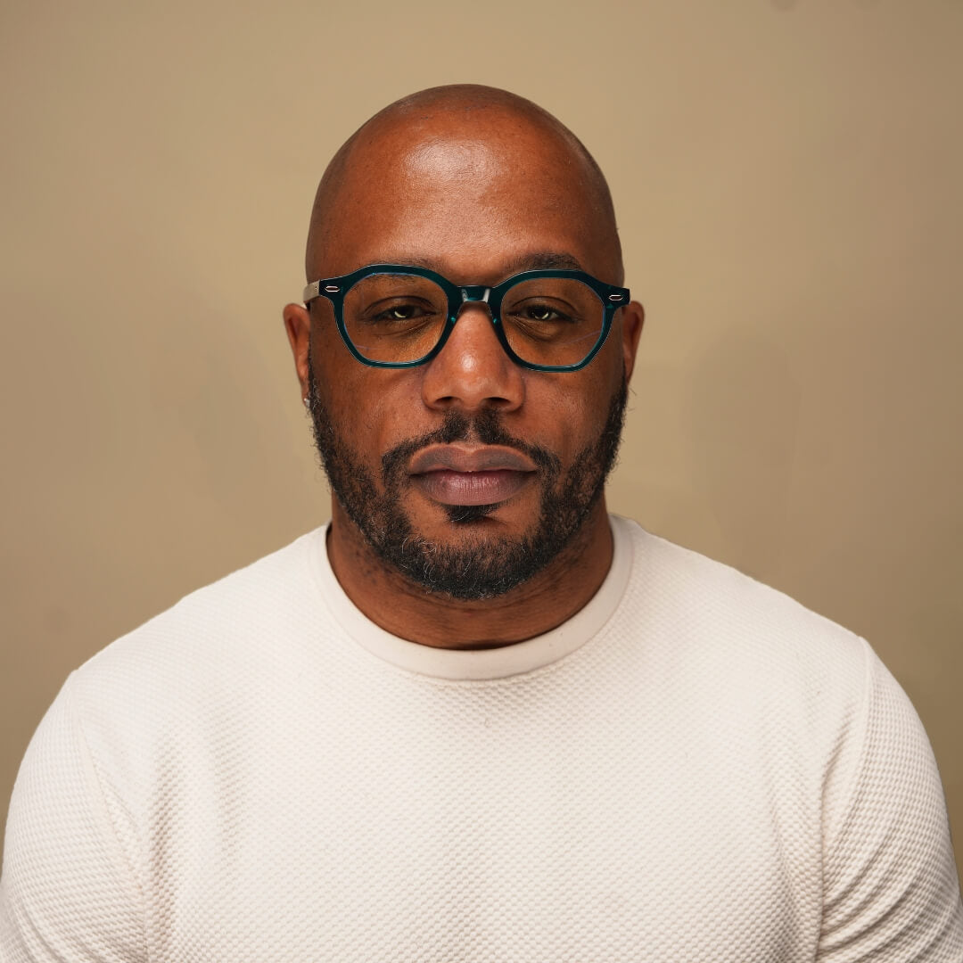 Man wearing glasses and a white sweater against a beige background