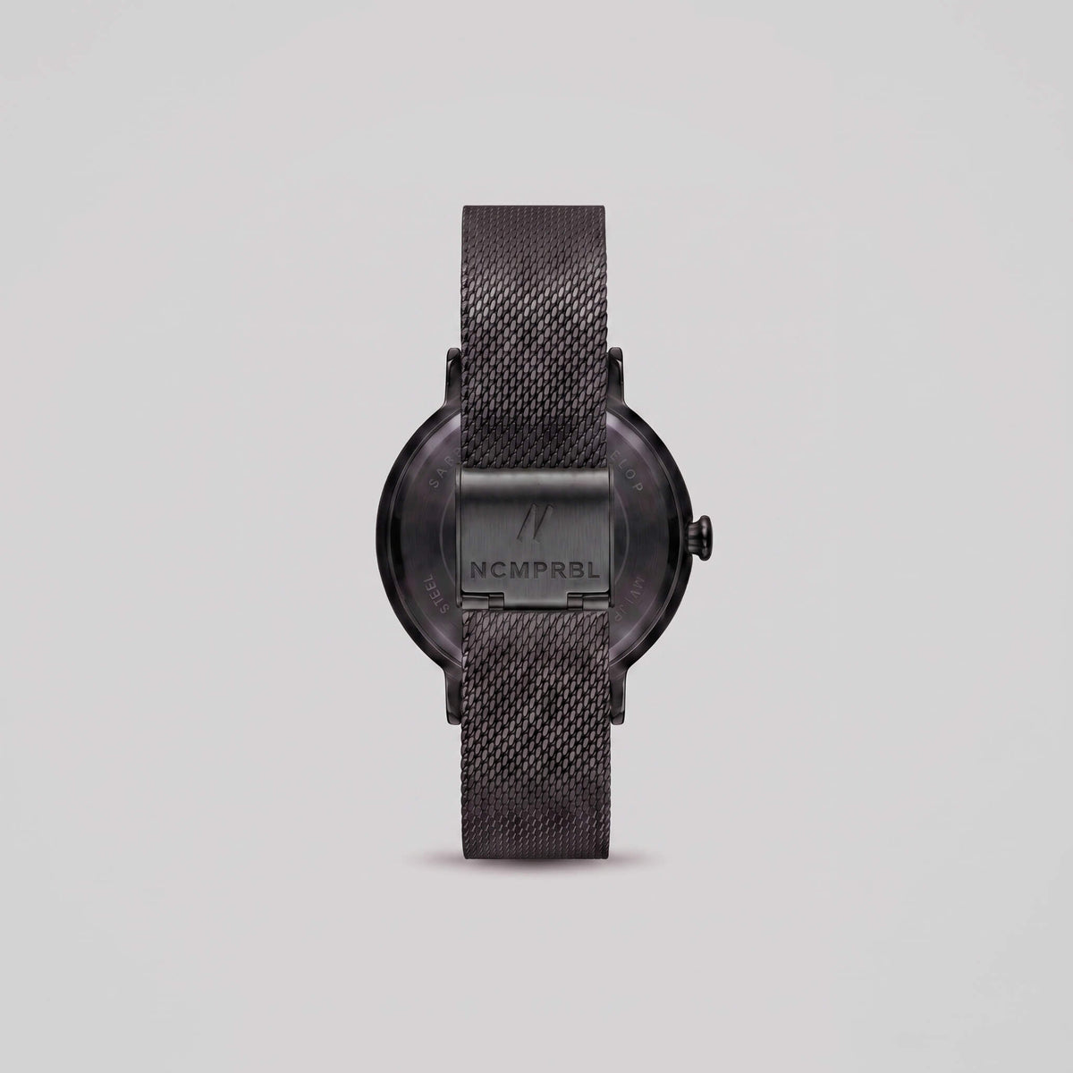 black mesh strap watch shown from the back, featuring a round case with a visible 'NCMPRBL' brand logo on the center band, set against a solid light gray background.