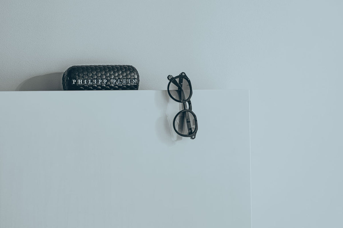 Close-up of stylish black glasses with a textured designer case on white background.